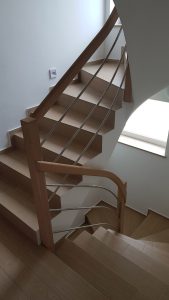 Lesena stopniščna ograja z okroglimi lineami za ročaj in ravne liee za inox ki povezuje lesene stebričke. Lesena romantika